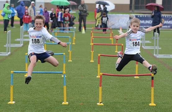 Zwei Kinder springen bei Regen gleichzeitig über die Kinderhürden